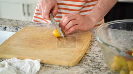 Photo for In the contemporary ambiance of a modern kitchen, a young man engages in dinner preparations. His current activity entails meticulously slicing small rainbow potatoes in half on a wooden cutting board - Royalty Free Image