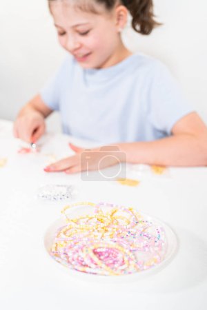 Photo for Little girl enjoys crafting colorful bracelets with vibrant clay beads set. - Royalty Free Image
