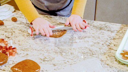 Téléchargez les photos : Utilisation d'un rouleau à pâtisserie réglable pour dérouler la pâte à biscuits au pain d'épice sur l'élégant comptoir en marbre dans une cuisine moderne, se préparer pour la cuisson de vacances festives. - en image libre de droit