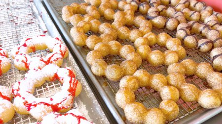 Téléchargez les photos : Donuts mochi fraîchement cuits avec diverses garnitures sur des plateaux métalliques, soulignant leur forme unique et revêtements sucrés. - en image libre de droit