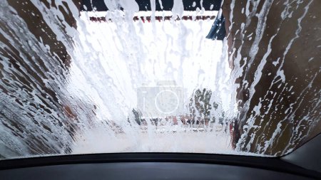 Foto de Vista del parabrisas jabonosa desde el interior de un coche durante un ciclo de lavado automático, con la espuma oscureciendo el exterior. - Imagen libre de derechos