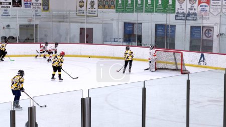 Photo for Denver, Colorado, USA-February 17, 2024-Young athletes in the midst of a lively hockey game, with players chasing the puck across the ice rink bordered by spectators. - Royalty Free Image