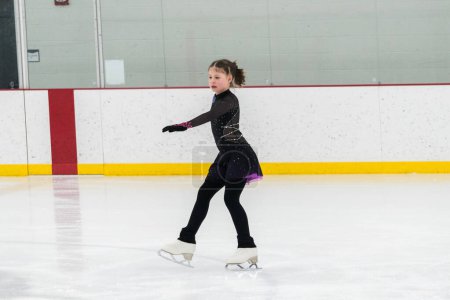 Photo for Young girl perfecting her figure skating routine while wearing her competition dress at an indoor ice rink. - Royalty Free Image
