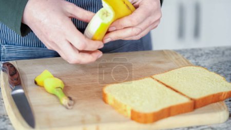 Foto de En una moderna cocina blanca, se preparan plátanos con mantequilla y pan brioche para hacer un delicioso sándwich de plátano con mantequilla de maní a la parrilla.. - Imagen libre de derechos