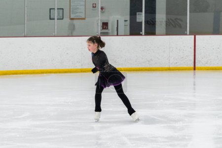 Téléchargez les photos : Jeune fille perfectionnant sa routine de patinage artistique tout en portant sa robe de compétition à une patinoire intérieure. - en image libre de droit