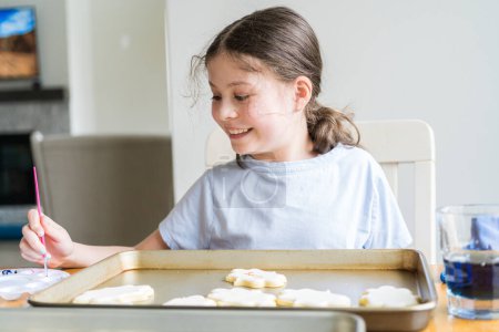 Photo for A heartwarming scene of a little girl carefully writing Sorry on sugar cookies with food coloring, the cookies beautifully flooded with white royal icing. - Royalty Free Image