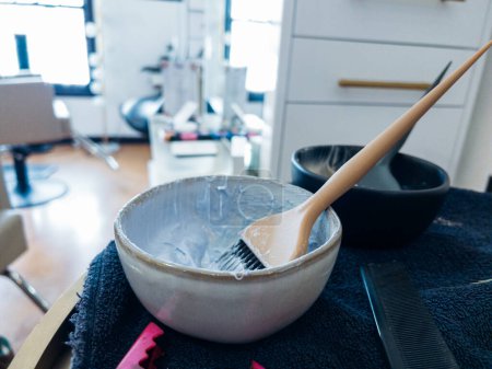 Photo for Rich, creamy hair dye mix rests on a wooden brush over a sleek bowl. The tools for hair coloring lie on a dark, textured towel, with a hint of vibrant pink peeking through, suggesting the lively work - Royalty Free Image