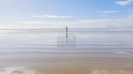 Téléchargez les photos : Petite fille, bravant le froid, court joyeusement dans son maillot de bain à travers la plage pendant l'hiver. - en image libre de droit