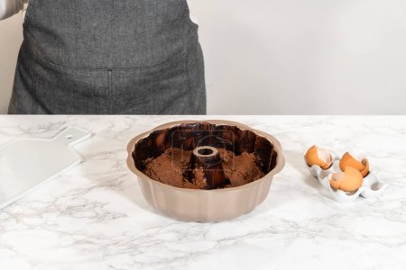 Téléchargez les photos : La pâte préparée est soigneusement remplie dans la casserole de bundt graissée - préparant le terrain pour un délicieux gâteau au bundt au chocolat. - en image libre de droit