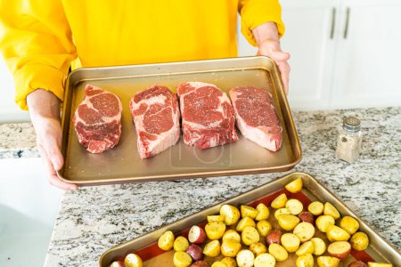 Photo for Situated in a modern white kitchen, a seasoned rib eye steak, boasting its beautiful marbling, sits ready on a baking sheet. It is prepared for the outdoor gas grill, promising a perfect sear on the - Royalty Free Image