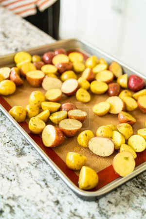 Photo for In a modern kitchen, an array of halved, multicolored marble potatoes are arranged on a baking pan lined with a silicone liner. The roasting process infuses the kitchen with a mouthwatering aroma - Royalty Free Image