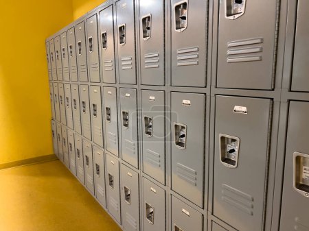 En un pasillo de la escuela, una serie uniforme de casilleros grises está listo para los estudiantes, los respiraderos y cerraduras que puntuaban las puertas de metal liso.