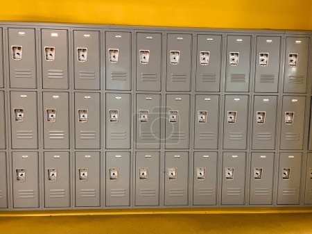 Foto de En un pasillo de la escuela, una serie uniforme de casilleros grises está listo para los estudiantes, los respiraderos y cerraduras que puntuaban las puertas de metal liso. - Imagen libre de derechos