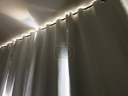 Téléchargez les photos : La lumière du soleil chaud filtre à travers les bords de lourds rideaux occultants, offrant une lueur tranquille dans l'espace calme d'une pièce reposante. - en image libre de droit