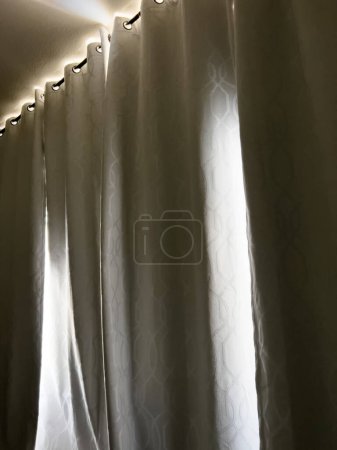 Foto de La cálida luz del sol se filtra a través de los bordes de las pesadas cortinas opacas, ofreciendo un brillo tranquilo en el espacio tranquilo de una sala de descanso.. - Imagen libre de derechos