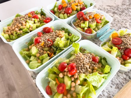 Containers filled with vibrant, nutritious salads are lined up on a kitchen counter, showcasing a colorful and healthful way to prepare for busy weekdays.