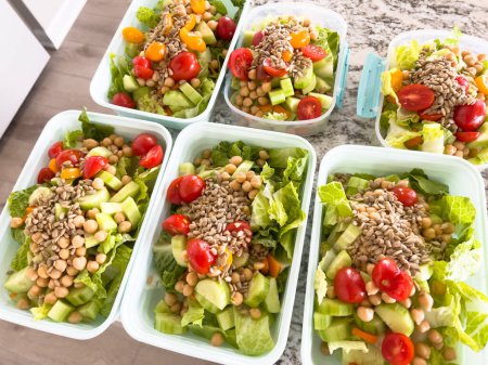 Containers filled with vibrant, nutritious salads are lined up on a kitchen counter, showcasing a colorful and healthful way to prepare for busy weekdays.