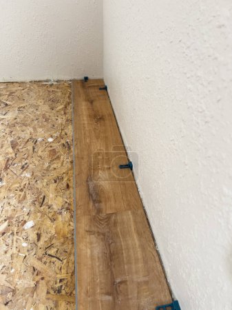 Photo for Carefully measured and evenly spaced, the first vinyl plank is expertly installed against the wall, marking the beginning of a transformative floor renovation. - Royalty Free Image