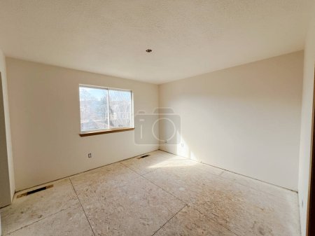 Bathed in natural sunlight, an empty room awaits new flooring, reflecting the initial stages of a home renovation project with its bare subfloors and freshly painted walls.
