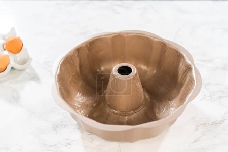 Using a silicone brush, the metal bundt cake pan is greased with melted vegetable shortening, preparing for baking the scrumptious Carrot Bundt Cake.