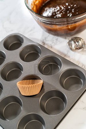 Getting ready to bake delicious chocolate cupcakes, we carefully line the cupcake pan with paper liners, ensuring a delightful treat awaits.