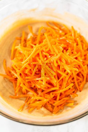 Téléchargez les photos : Dans un grand bol en verre, les ingrédients sont savamment mélangés pour créer la pâte pour la cuisson du délicieux gâteau Bundt aux carottes. - en image libre de droit