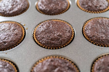 Just out of the oven, these delectable chocolate cupcakes are now resting and cooling on the kitchen counter, filling the air with their tempting aroma.