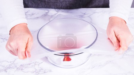 Téléchargez les photos : Les fraises, fraîchement lavées et séchées, sont soigneusement stockées dans un bol en verre doublé d'une serviette en papier et recouvertes d'une pellicule plastique pour maintenir leur fraîcheur.. - en image libre de droit