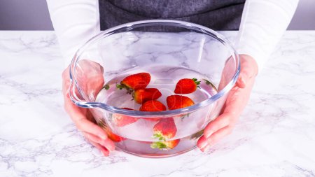 Photo for Ripe strawberries are submerged in water within a large glass mixing bowl, a step in washing the fruit to ensure cleanliness and longevity before storage or consumption. - Royalty Free Image