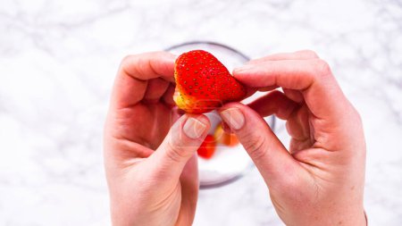 Téléchargez les photos : Pose plate. Les fraises, fraîchement lavées et séchées, sont soigneusement stockées dans un bol en verre doublé d'une serviette en papier et recouvertes d'une pellicule plastique pour maintenir leur fraîcheur.. - en image libre de droit