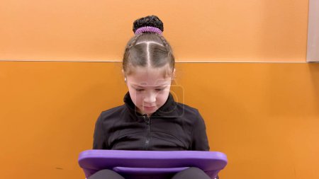 Photo for Nestled in a quiet hallway, this dedicated young figure skater finds a moment of tranquility, engrossed in her tablet as she mentally prepares for her upcoming performance. - Royalty Free Image