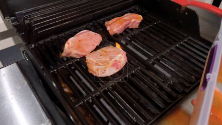Las chuletas frescas de cerdo están adornadas con la mezcla perfecta de condimentos mientras se cocinan a la perfección, con toques de marcas de focas doradas del calor de una parrilla de gas al aire libre..