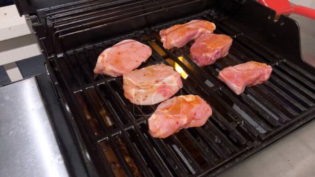 Frische Schweinekoteletts sind mit der perfekten Mischung aus Gewürzen geschmückt, während sie perfekt garen, mit einem Hauch von goldenen Searmarks aus der Hitze eines Outdoor-Gasgrills.