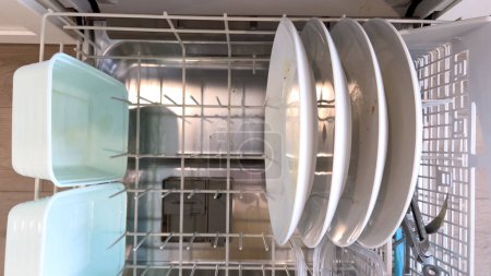 Die Aufgabe, eine Geschirrspülmaschine mit schmutzigem Geschirr zu beladen, wird hier erfasst, wobei der Schwerpunkt auf einer Schüssel mit Essensresten und verschiedenen Utensilien liegt, die eine übliche häusliche Routine hervorhebt..