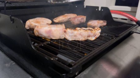 Téléchargez les photos : Côtelettes de porc frais sont ornés du mélange parfait d'assaisonnement comme ils cuisinent à la perfection, avec des notes de marques de saisir doré de la chaleur d'un barbecue à gaz extérieur. - en image libre de droit