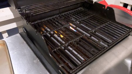 Photo for A well-prepared grilling surface awaits as the red silicone brush sweeps across the grill grates, an essential step in the preheating and cleaning process to ensure an even cooking experience. - Royalty Free Image