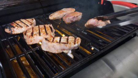 Frische Schweinekoteletts sind mit der perfekten Mischung aus Gewürzen geschmückt, während sie perfekt garen, mit einem Hauch von goldenen Searmarks aus der Hitze eines Outdoor-Gasgrills.