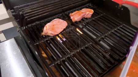 Photo for Fresh pork chops are graced with the perfect blend of seasoning as they cook to perfection, with hints of golden sear marks from the heat of an outdoor gas grill. - Royalty Free Image