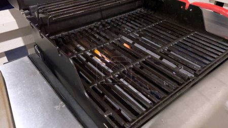 Photo for A well-prepared grilling surface awaits as the red silicone brush sweeps across the grill grates, an essential step in the preheating and cleaning process to ensure an even cooking experience. - Royalty Free Image