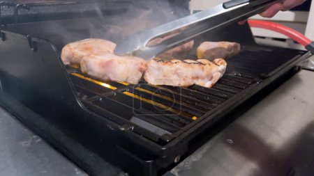 Las chuletas frescas de cerdo están adornadas con la mezcla perfecta de condimentos mientras se cocinan a la perfección, con toques de marcas de focas doradas del calor de una parrilla de gas al aire libre..