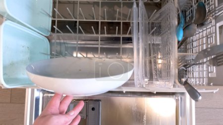 The task of loading a dishwasher with dirty dishes is captured here, with a focus on a bowl with food residue and various utensils, highlighting a common domestic routine.