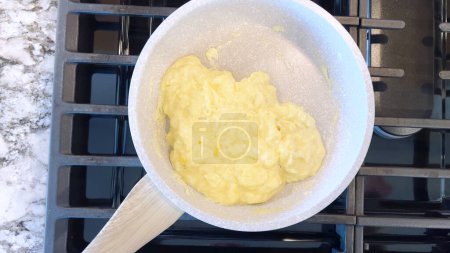 Téléchargez les photos : Main tient une spatule rouge, en remuant des œufs brouillés brillants dans une poêle antiadhésive, la flamme bleue d'une cuisinière à gaz en dessous assurant un repas chaud et copieux. - en image libre de droit