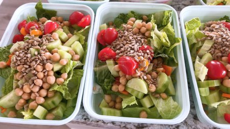 Los recipientes llenos de ensaladas vibrantes y nutritivas se alinean en un mostrador de cocina, mostrando una manera colorida y saludable de prepararse para los días laborables ocupados..
