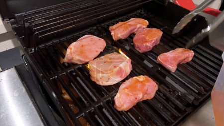 Téléchargez les photos : Côtelettes de porc frais sont ornés du mélange parfait d'assaisonnement comme ils cuisinent à la perfection, avec des notes de marques de saisir doré de la chaleur d'un barbecue à gaz extérieur. - en image libre de droit
