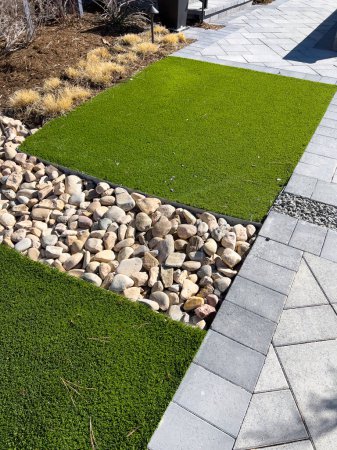 Photo for The modern landscaping design features vibrant artificial turf contrasting with natural pebbles and structured pavers, offering a low-maintenance yet aesthetically pleasing outdoor space. - Royalty Free Image