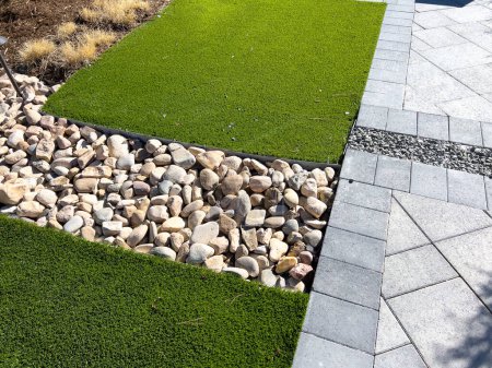 The modern landscaping design features vibrant artificial turf contrasting with natural pebbles and structured pavers, offering a low-maintenance yet aesthetically pleasing outdoor space.