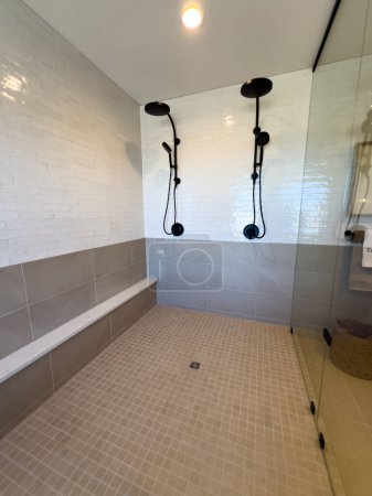 Elegantly designed walk-in shower, equipped with dual matte black shower heads and a built-in bench. The contrasting white subway tiles and grey accents give the space a modern and clean aesthetic.