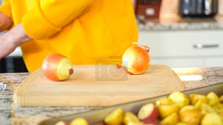 Im einladenden Ambiente einer modernen Küche setzt ein junger Mann seine Essenszubereitung fort. Derzeit schneidet er gelbe Zwiebeln in Ringe und bereitet sie zum Grillen auf einem Grill vor