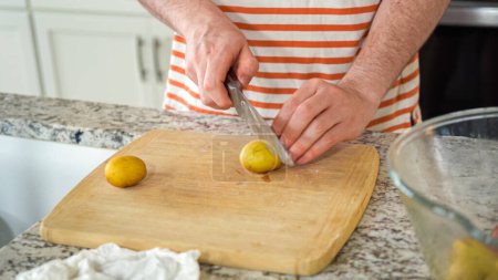 In the contemporary ambiance of a modern kitchen, a young man engages in dinner preparations. His current activity entails meticulously slicing small rainbow potatoes in half on a wooden cutting board