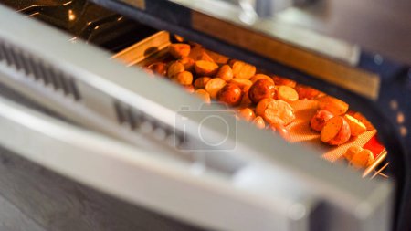 Photo for Within the setting of a modern kitchen, a young man is immersed in preparing dinner, currently roasting seasoned rainbow potatoes in the oven, an important step towards a delightful meal. - Royalty Free Image